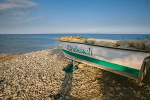 a boat sitting on a rocky beach next to the ocean at Elya Beach Luxury Suites in Ayios Theodhoros