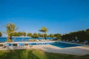 a swimming pool with chairs and the ocean in the background at Elya Beach Luxury Suites in Ayios Theodhoros