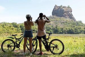 two people standing next to bikes in a field at Jungle Trails in Sigiriya
