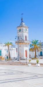 a clock tower in front of a building with palm trees at Almurigini I Boutique House I Ceglie Messapica in Ceglie Messapica