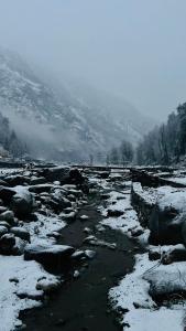 a river with snow on the rocks and a mountain at Mahi camping & cottages in Jagatsukh