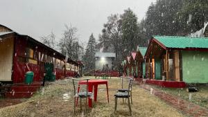 a group of chairs and a red table in the snow at Mahi camping & cottages in Jagatsukh +3 photos