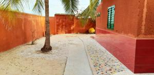 a palm tree next to a red building with a sidewalk at Oasis Palmarin in Palmarin +6 photos