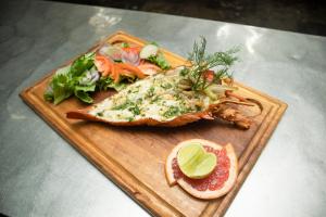 a fish on a wooden cutting board with a salad at GINFORM at Hotel Petit Brussel in Lomé