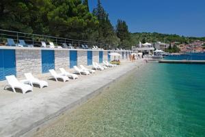 a row of white lounge chairs next to a body of water at Keti House Rooms in Vela Luka