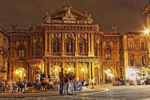 a large building with people standing outside of it at night at La Maison Du Theatre in Catania