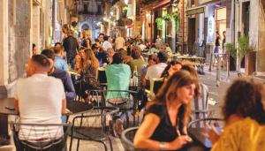 a crowd of people sitting at tables in an alley at La Maison Du Theatre in Catania