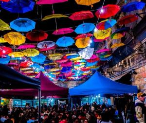 a crowd of people under colorful umbrellas hanging from ceilings at La Maison Du Theatre in Catania