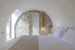 a bedroom with a white bed and a stone wall at Maiandros Suites in Karterados +95 photos