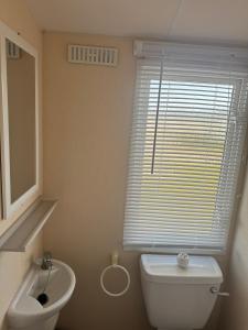 a bathroom with a toilet and a sink and a window at Golden Anchor 6 Berth Caravan, Chapel St Leonards, 22 Wild Flower Meadow in Chapel Saint Leonards +22 photos