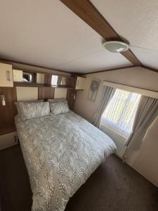 a bed in a small room with a window at Golden Anchor 6 Berth Caravan, Chapel St Leonards, 22 Wild Flower Meadow in Chapel Saint Leonards