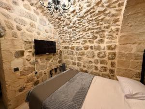a bedroom with a stone wall with a bed and a tv at Sümerler Konağı in Mardin
