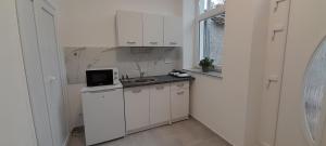 a small kitchen with white cabinets and a microwave at Déri Kert Apartmanház B in Baja