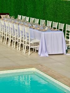 a long table with white chairs and a pool of water at Vikendoria Pool House & Events in Bački Jarak +6 photos