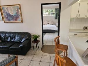 a living room with a black leather couch and a bedroom at Leopards Tree Garden Cottage in Greytown