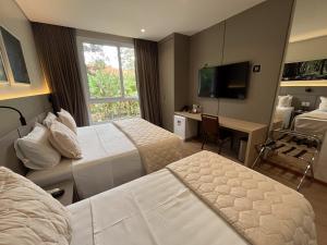 a hotel room with two beds and a desk and a television at Hotel Pousada do Bosque in Ponta Porã