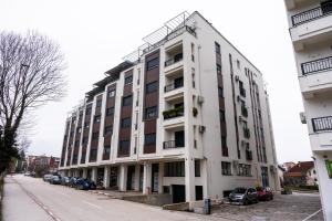 a white building with cars parked in a parking lot at Aura Apartmani Vrnjačka Banja in Vrnjci