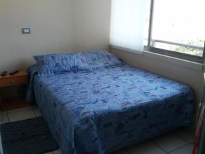 1 dormitorio con 1 cama con edredón azul y ventana en Coraceros Apartment, en Viña del Mar