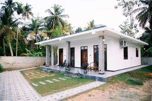 a small white house with palm trees in the background at Paddy Breeze Villa in Batigama