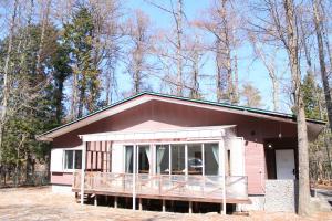 a small pink house with a porch in the woods at 彩の宿月屋 in Yamanakako