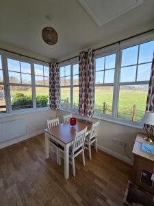 a dining room with a table and chairs and windows at Wagtail Cottage in Kilmartin