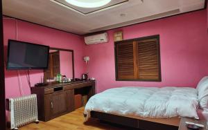 a bedroom with a pink wall with a bed and a tv at 필모텔 in Yeoju