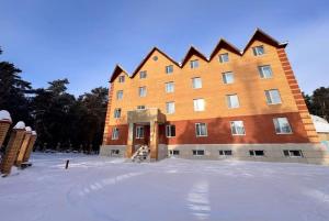 a large brick building with snow in front of it at Hotel Nurlytau in Borovoye