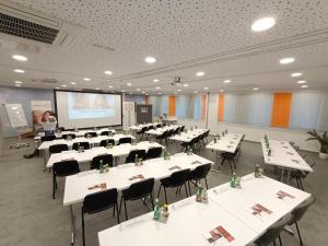 a conference room with white tables and chairs and a screen at AIS Center in Wolfsberg