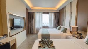 a hotel room with two beds and a flat screen tv at Enrich Grand Hotel in Bangkok