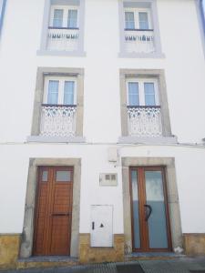 a white building with two doors and two windows at LA CASINA DE HUGO AZUL centro Luanco in Luanco