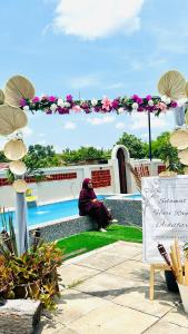 a person sitting on the grass next to a pool at Homestay Babah - Private Chalet in Malacca