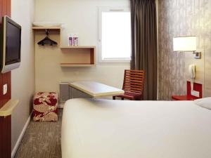 a hotel room with a bed and a desk and a tv at ibis Styles Ouistreham in Ouistreham