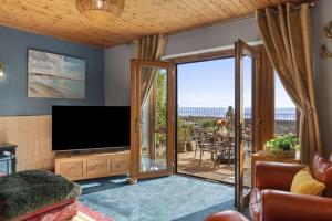 a living room with a television and a balcony at Bay View - holiday cottage by the sea with stunning views in Pendine
