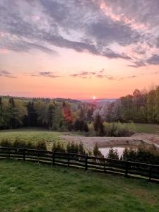 a sunset over a field with a fence and a river at Dom na Krzemienicy in Izdebki