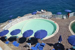 a swimming pool with blue umbrellas and the ocean at Magic View in Tuscany in Capo D'Arco