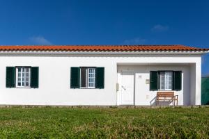 a white house with green shutters and a chair at Casa do Lado, Flores Açores in Lajes das Flores