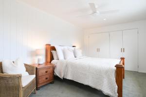 a white bedroom with a bed and a chair at The Salt Shack in Mallacoota