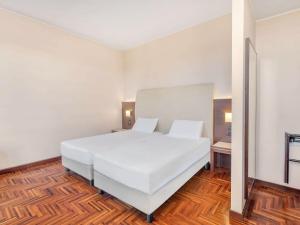 a bedroom with a white bed and a wooden floor at B&B HOTEL Habitat Giussano in Giussano