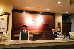 Dois homens atrás de um balcão no átrio de um hotel. em Hotel New Station em Matsumoto