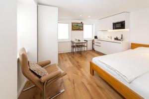 a bedroom with a bed and a chair and a kitchen at Herti14 Serviced Apartments in Ennetbaden