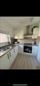 a kitchen with white cabinets and a sink and a stove at Dove Cottage in Greenock