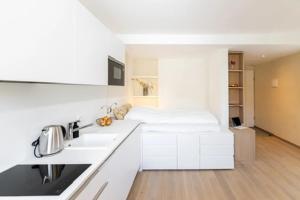 a white kitchen with a bed in the background at Herti14 Serviced Apartments in Ennetbaden