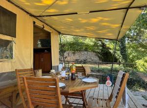 a patio with a wooden table and chairs under a tent at Camping Le Soleil du Verdon in Esparron-de-Verdon