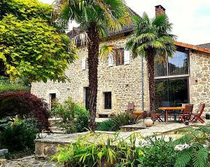a stone house with a table and two palm trees at Domaine Le Verger Kleinschalige B&B met groot zwembad en buitenkeuken in Saint-Estèphe