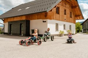 four girls riding on toy cars in front of a barn at Feriendorf Edelweiss in Mariapfarr