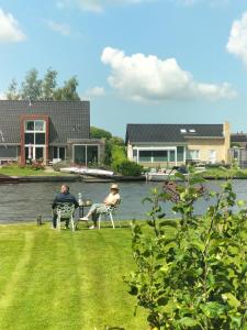 two people sitting in chairs on a lawn by the water at Havenkantoortje in Woudsend