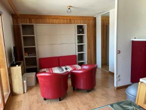 a living room with a table and two red chairs at La Marmotte ensoleillée in Montclar +3 photos