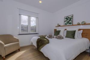 a white bedroom with a large bed and a chair at Nono Guest House in Ribeira Grande
