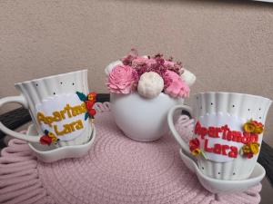 two coffee cups and a vase with flowers in it at Apartman LARA in Pirot
