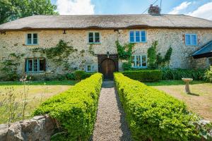 an old stone house with hedges in front of it at Berehayes Farmhouse in Bridport